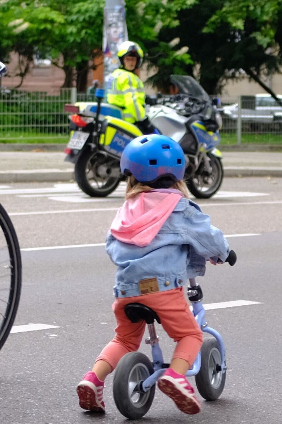 Kidical_Mass_07.2021_copyright_ADFC_BW_oder_Kidical_Mass_Stuttgart__21_ Mutter mit Kind auf der Straße. im Hintergrund ist ein Polizist zu sehen.