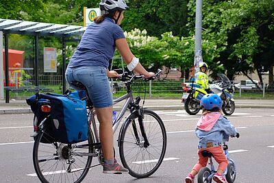 Mutter mit Kind auf der Straße. im Hintergrund ist ein Polizist zu sehen. 