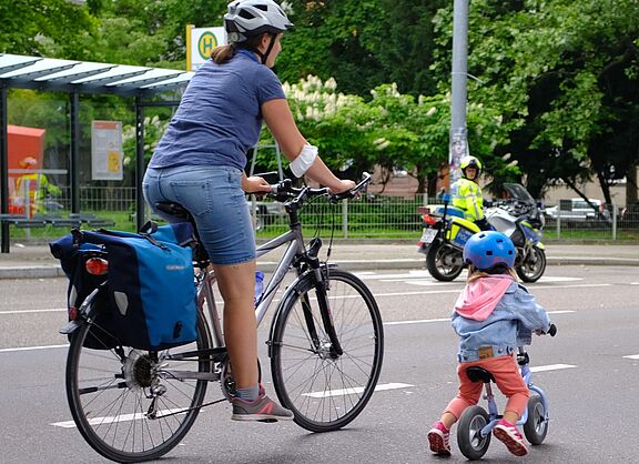 Mutter mit Kind auf der Straße. im Hintergrund ist ein Polizist zu sehen. 