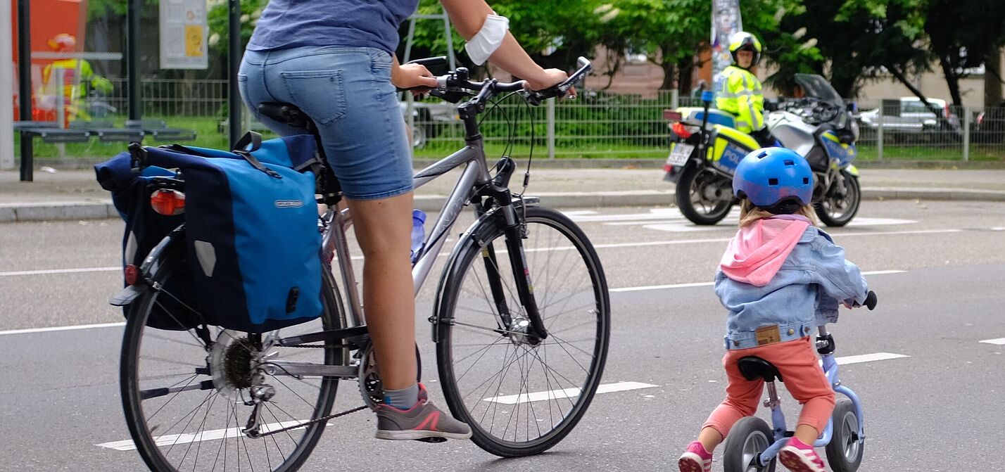 Mutter mit Kind auf der Straße. im Hintergrund ist ein Polizist zu sehen. 