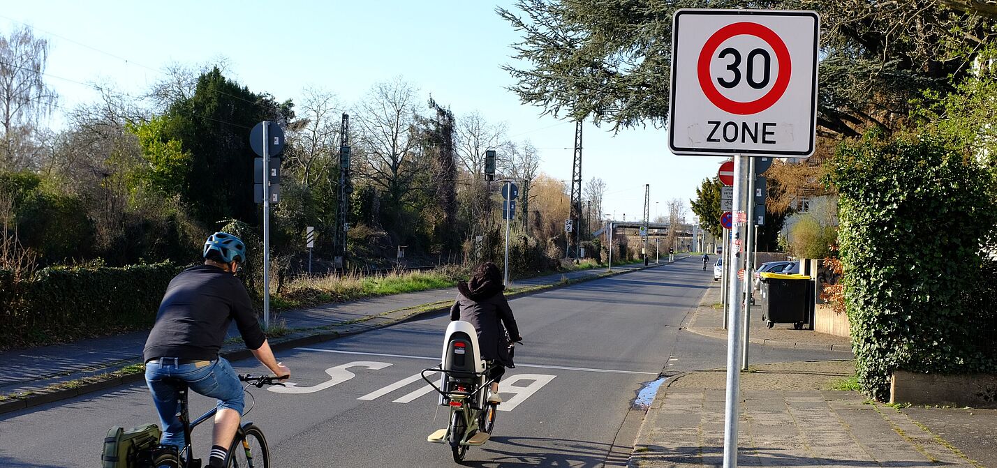 Zwei Radfahrer fahren an einem Tempo 30 Schild vorbei. 
