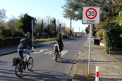 Zwei Radfahrer fahren an einem Tempo 30 Schild vorbei. 