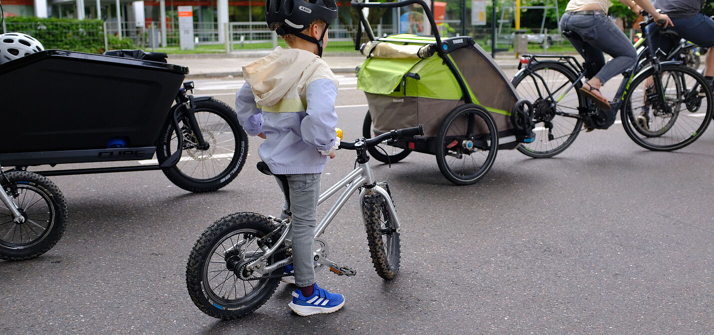 Ein Kind mit Fahrrad und Eltern mit Radanhänger und Lanstenrad sind auf dem Bild zu sehen.