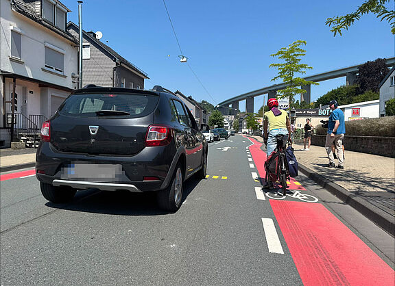 Eine Person im Auto überholt einen Radfahrer in Siegen-Eiserfeld auf der Eiserfelder Straße.
