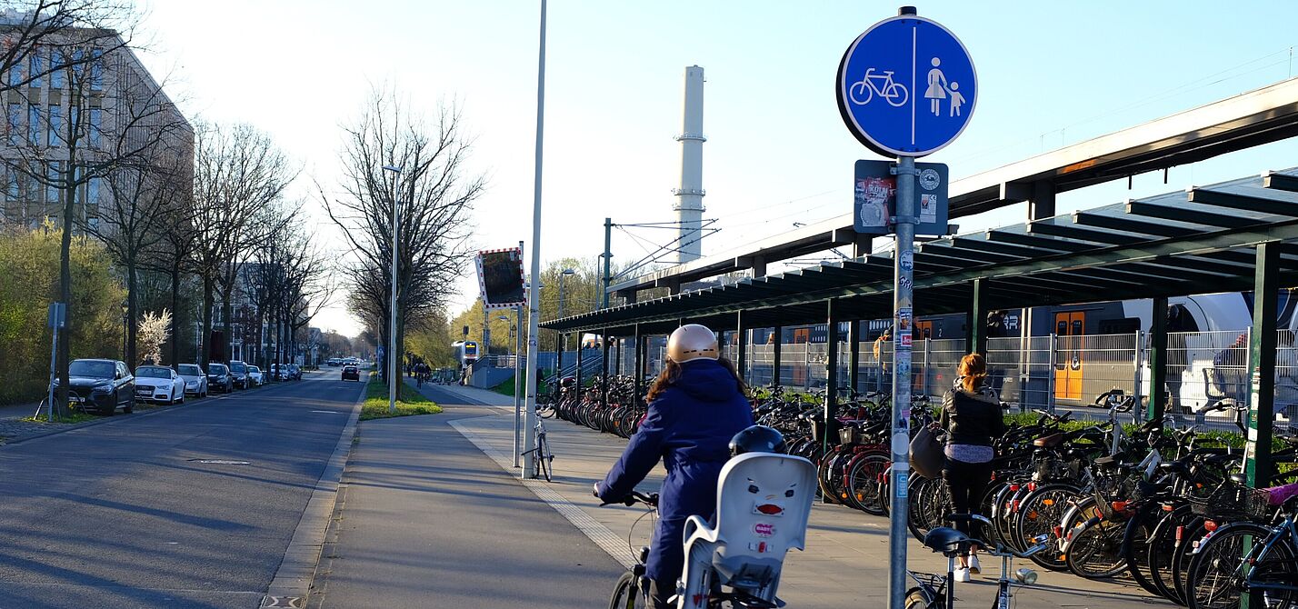 Bahnhalt, Regionalbahn, Radabstellanlage und eine Radfahrerin. 
