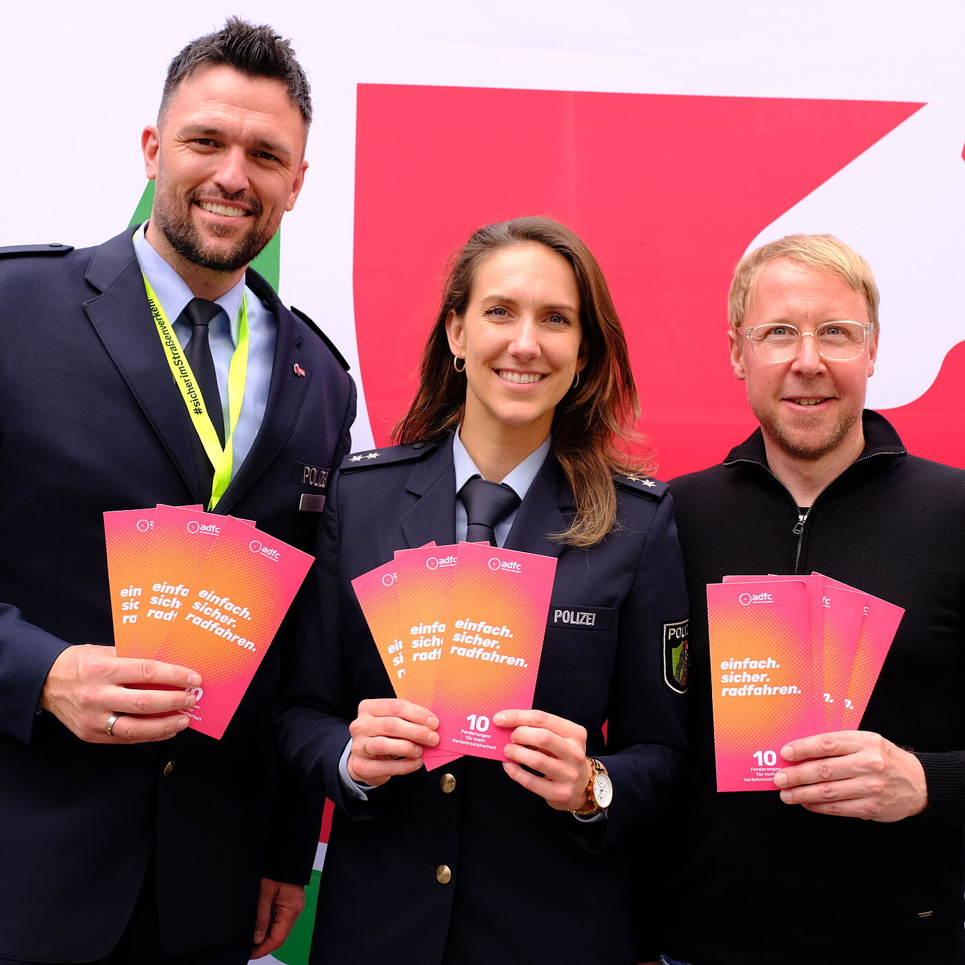 Eine Polizistin , ein Polizist und ein Mitarbeiter des ADFC halten Flyer hoch. 